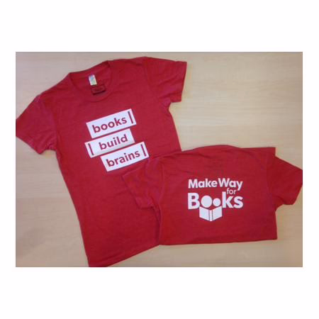 Two red T-shirts laid flat. The larger shirt reads “books build brains!” and the smaller shirt reads “Make Way for Books” above an open-book logo.